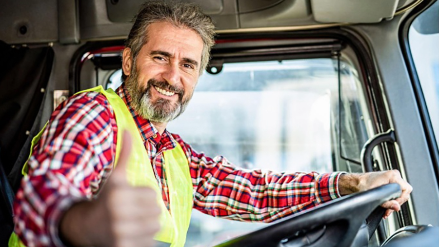 Male with red plaid shirt sitting in driver seat of semi truck with yellow safety vest on