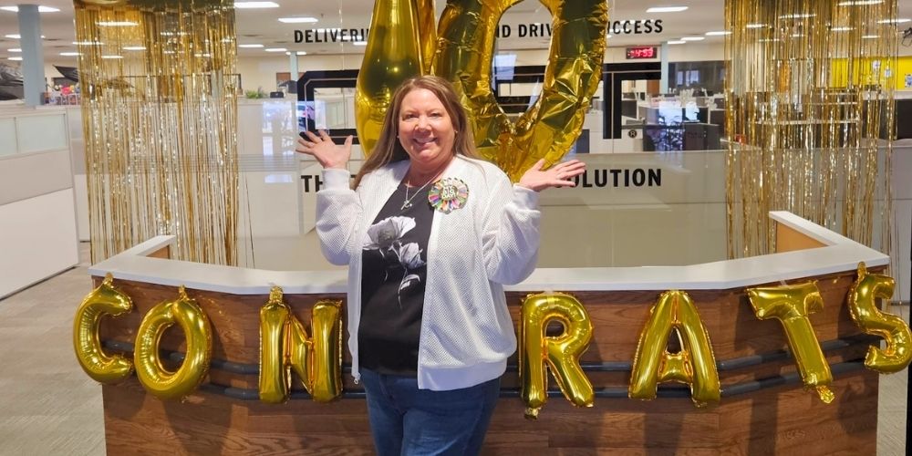 Therese Strellner poses with large gold balloons spelling “40” and “CONGRATS” at the CRST front desk, celebrating four decades of service.