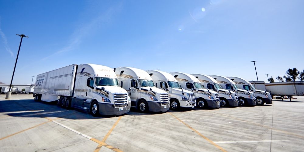 A row of white CRST semi-trucks parked neatly in a lot under a clear blue sky.
