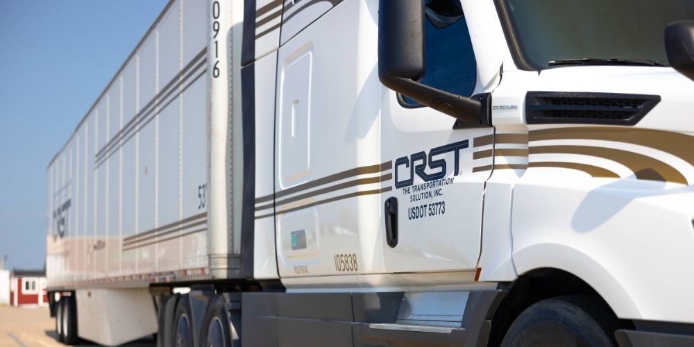 Close-up of a CRST semi-truck with branded trailer, parked under clear blue skies.