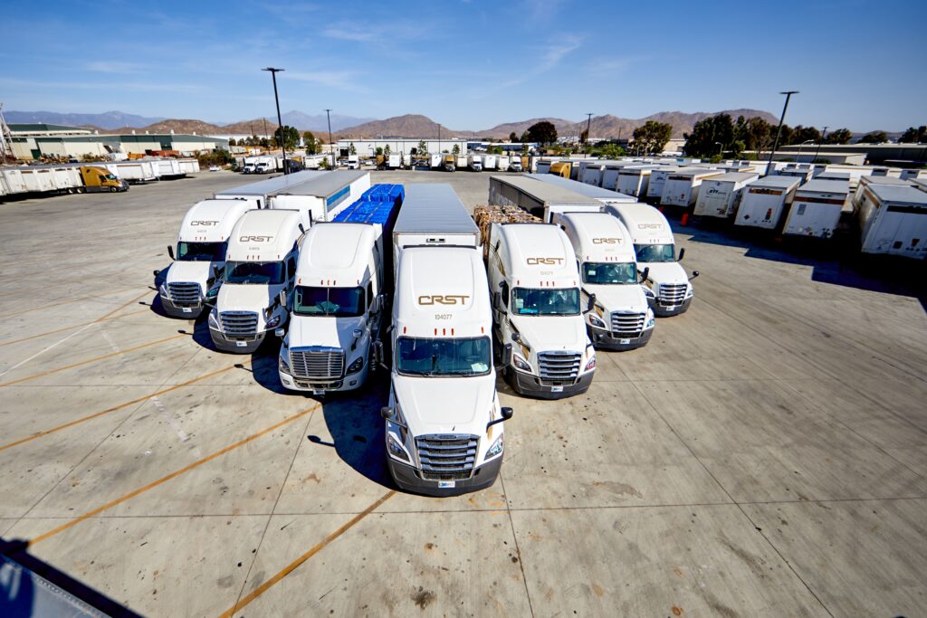 CRST Dedicated tractors and trailers positioned in a fleet yard, representing dedicated transportation services and private fleet conversion solutions for shippers.