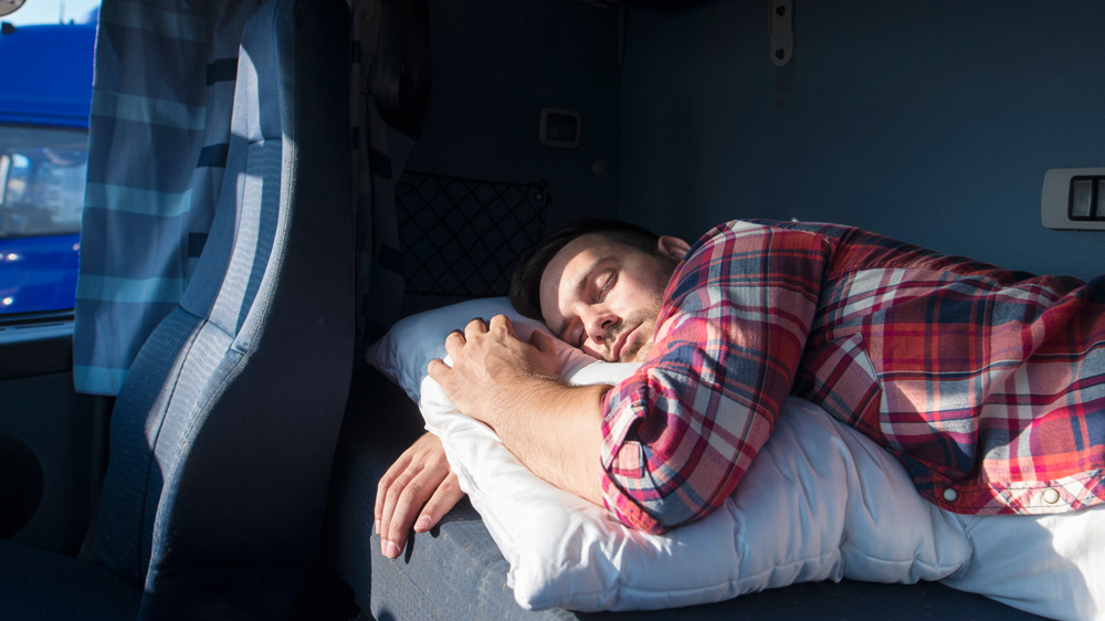 Truck driver napping in a sunlit sleeper berth, a reminder that daylight saving time and sleep go hand in hand