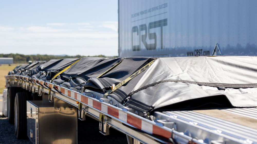 CRST flatbed trailer with tarped, strapped cargo and CRST dry van in background